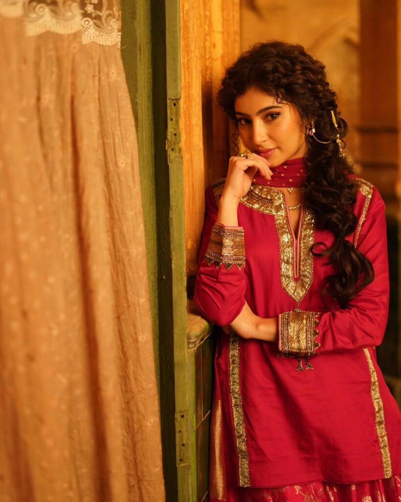 Sara Arjun wearing a rose pink embroidered kurta with matching dupatta and sharara, styled in a traditional indoor setting with warm lighting.